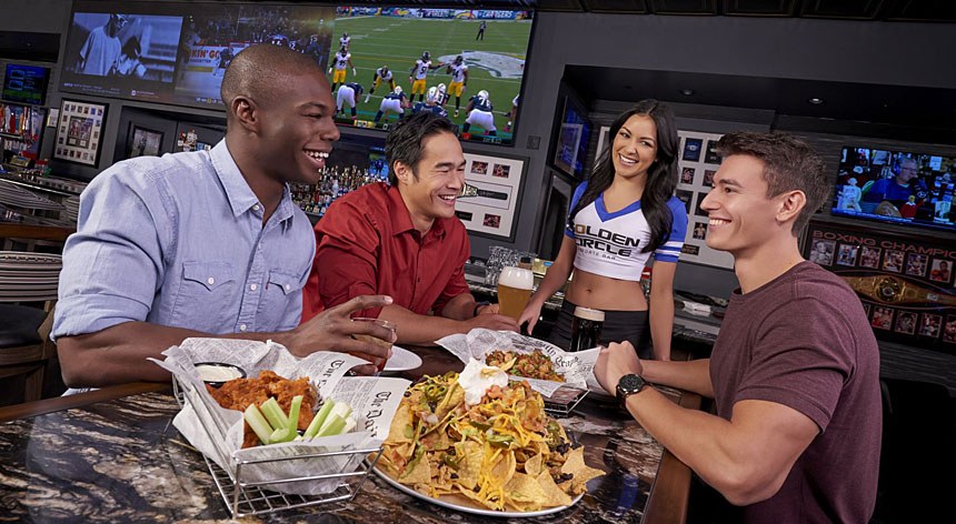 Golden Circle Sportsbook & Bar guests and server at table with nachos and wings